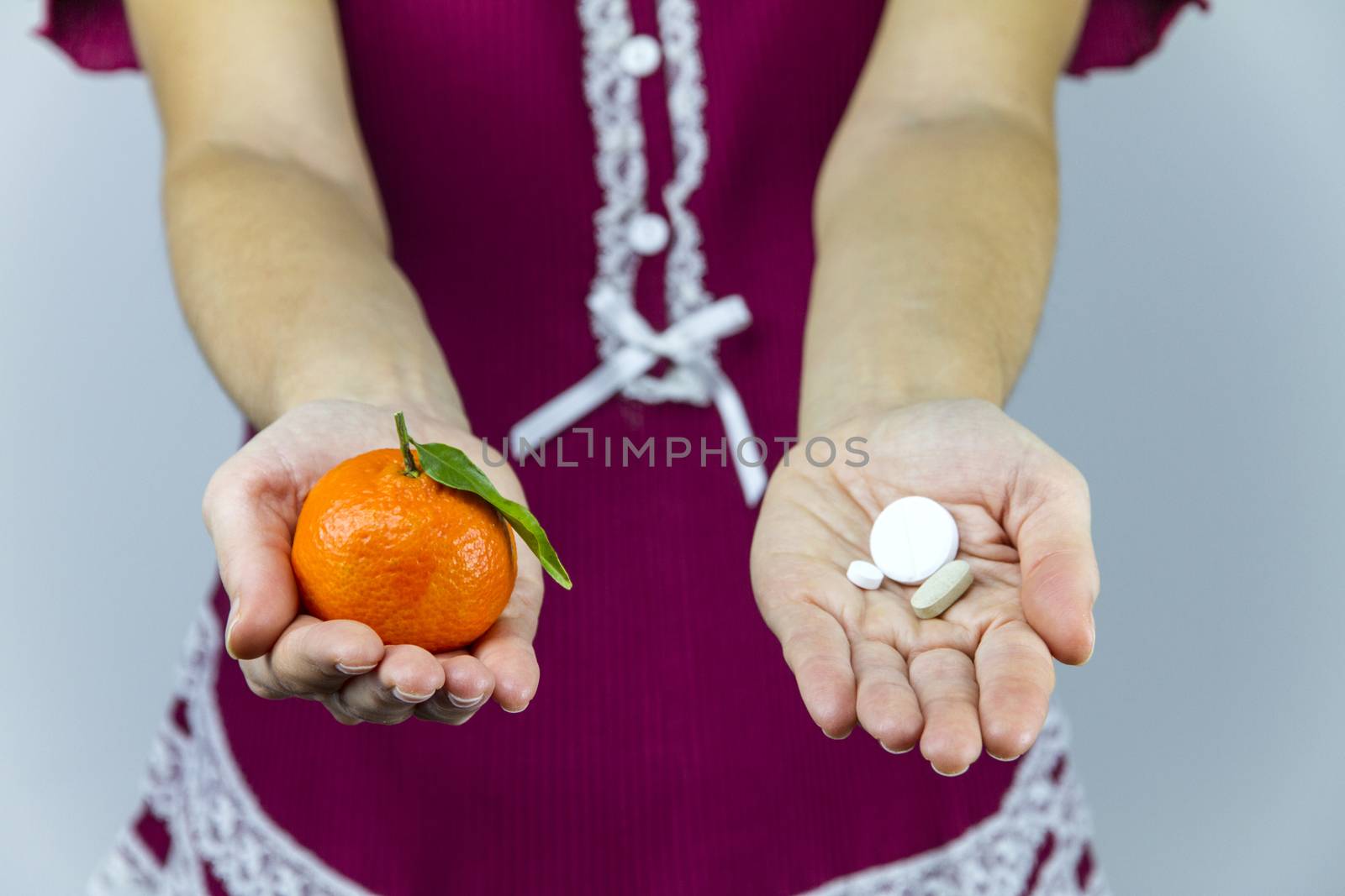Vitamins from fruits or medicines? A young woman in burgundy pajamas shows a mandarin in her right hand and an aspirin in her left