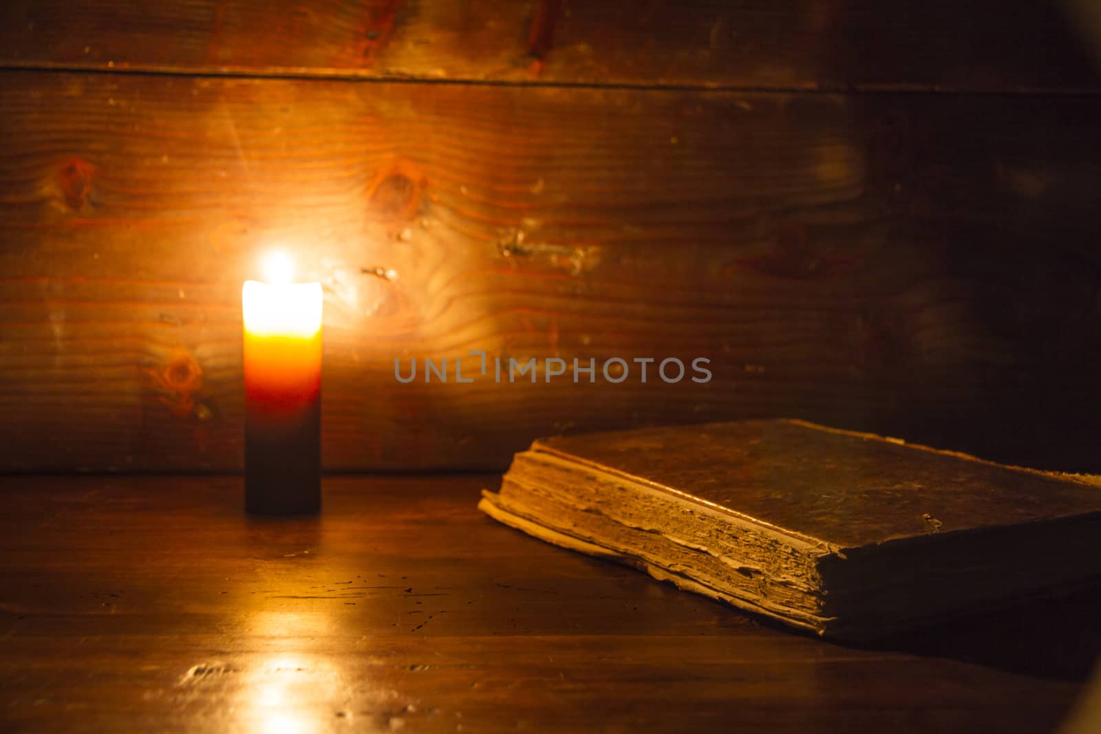 Reading scene in ancient times: an old book leaning on ruined wooden table lighted by a candle on a wooden background