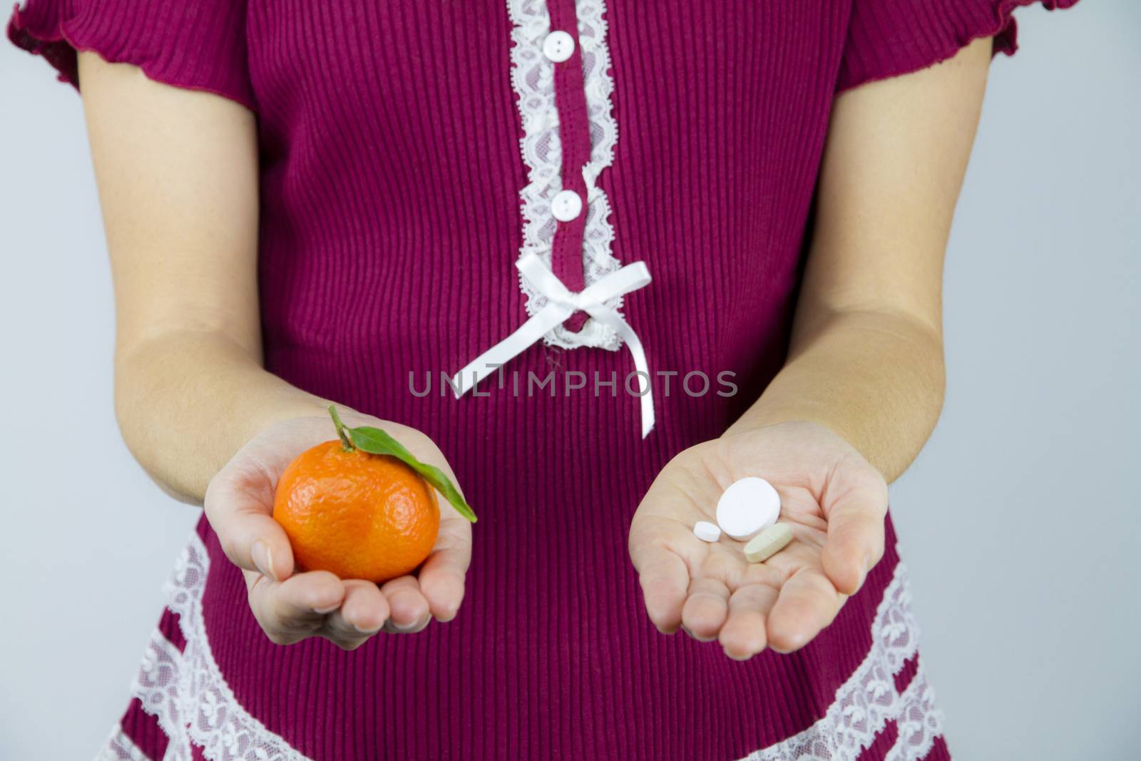 Vitamins from fruits or medicines? A young woman in burgundy pajamas shows a mandarin in her right hand and an aspirin in her left