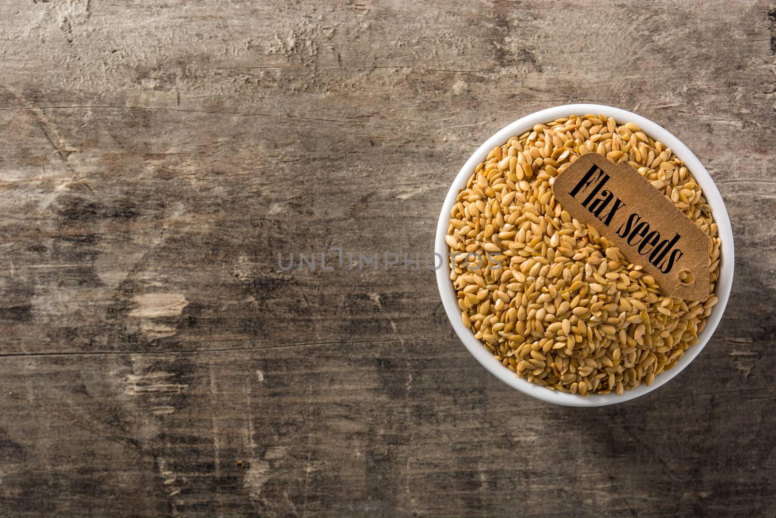 Golden flax seeds in white bowl on wooden table