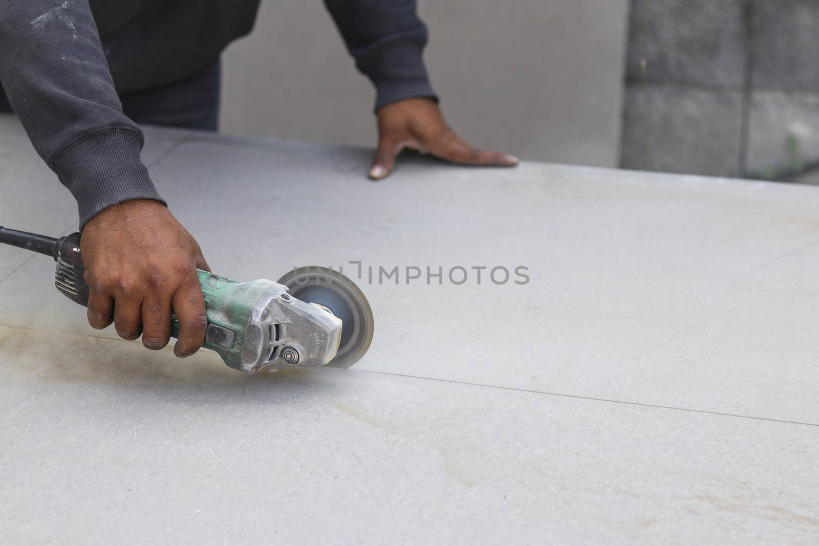 The mechanic is using a grinding machine for cut in half of cement board.