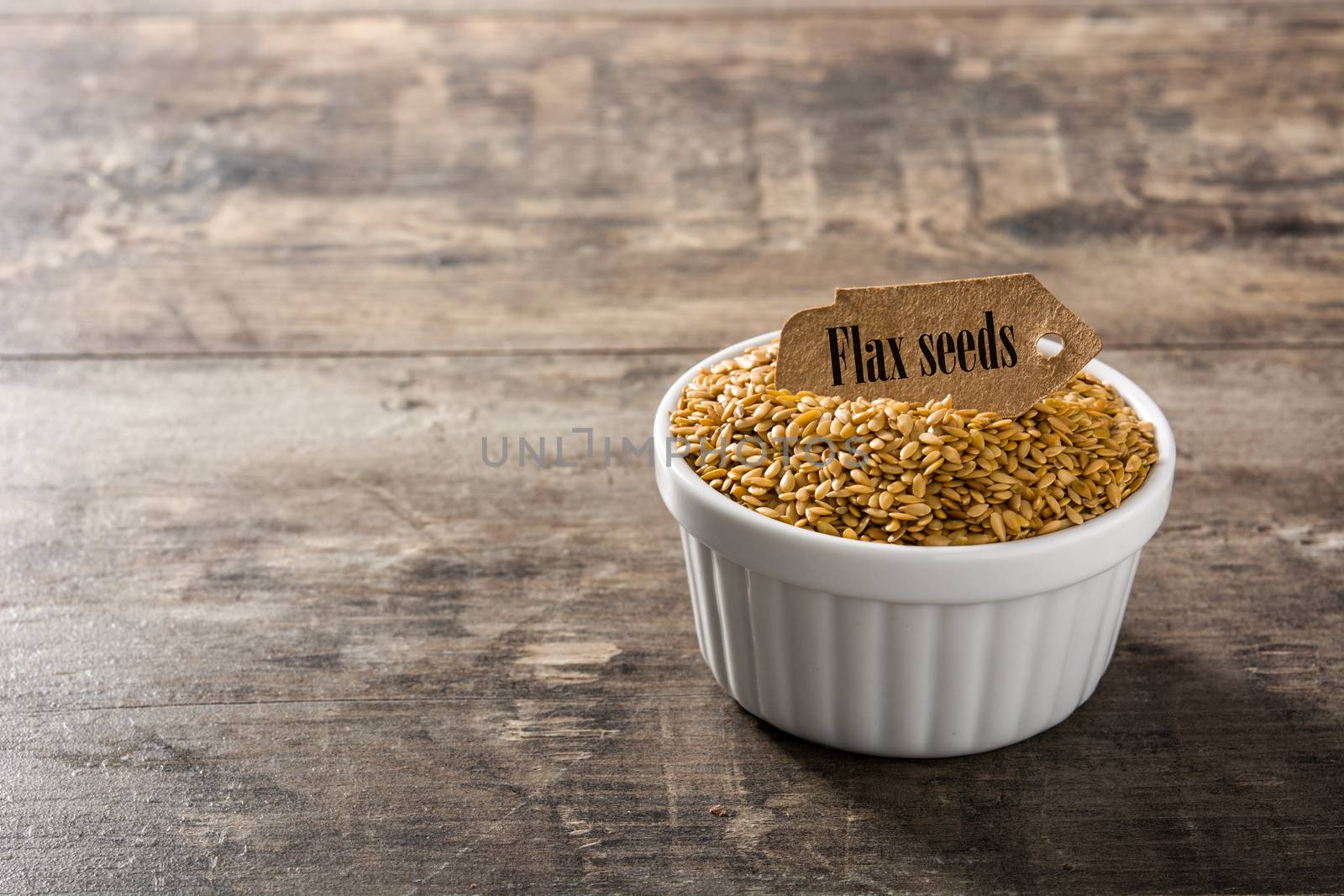 Golden flax seeds in white bowl on wooden table