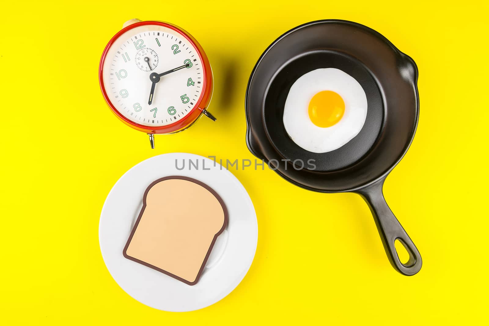 Frying pan with fried egg and alarm clock isolated on a yellow background viewed from above.Concept of breakfast at the race against time.