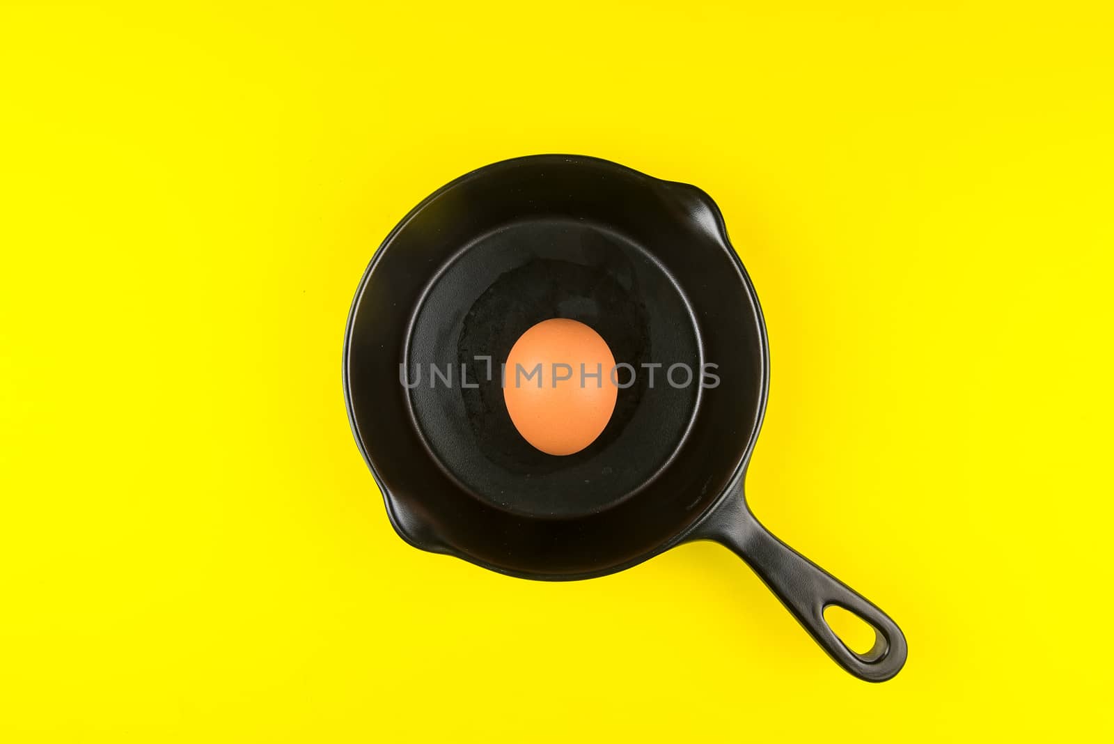 Top view of raw chicken eggs in frying pan on yellow background. by Bubbers