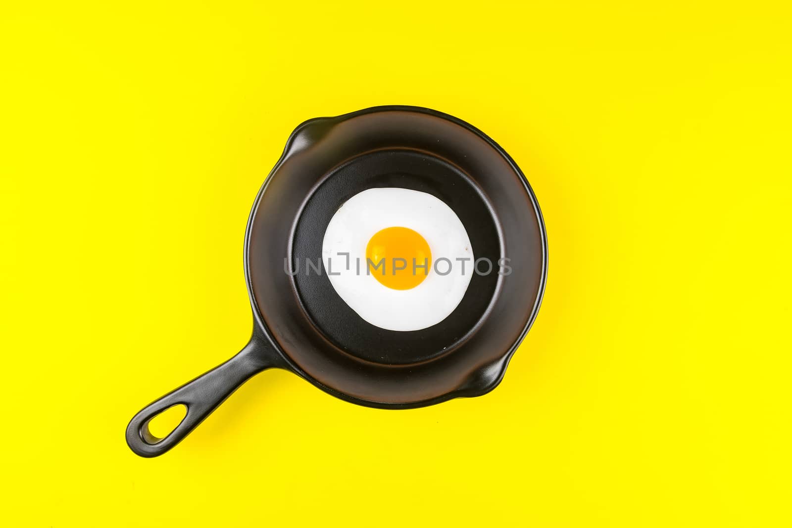 Frying pan with fried egg isolated on a yellow background viewed from above.