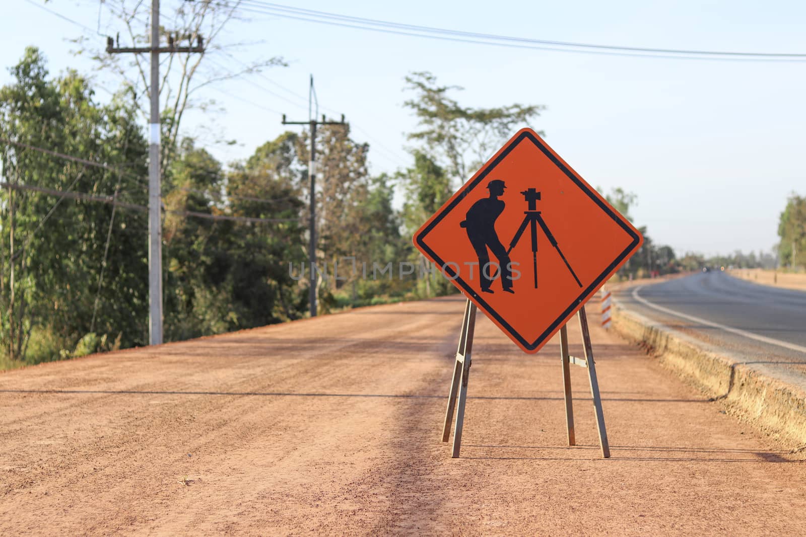 Orange label with pictograms survey engineering inside placed along the road under construction. by Eungsuwat