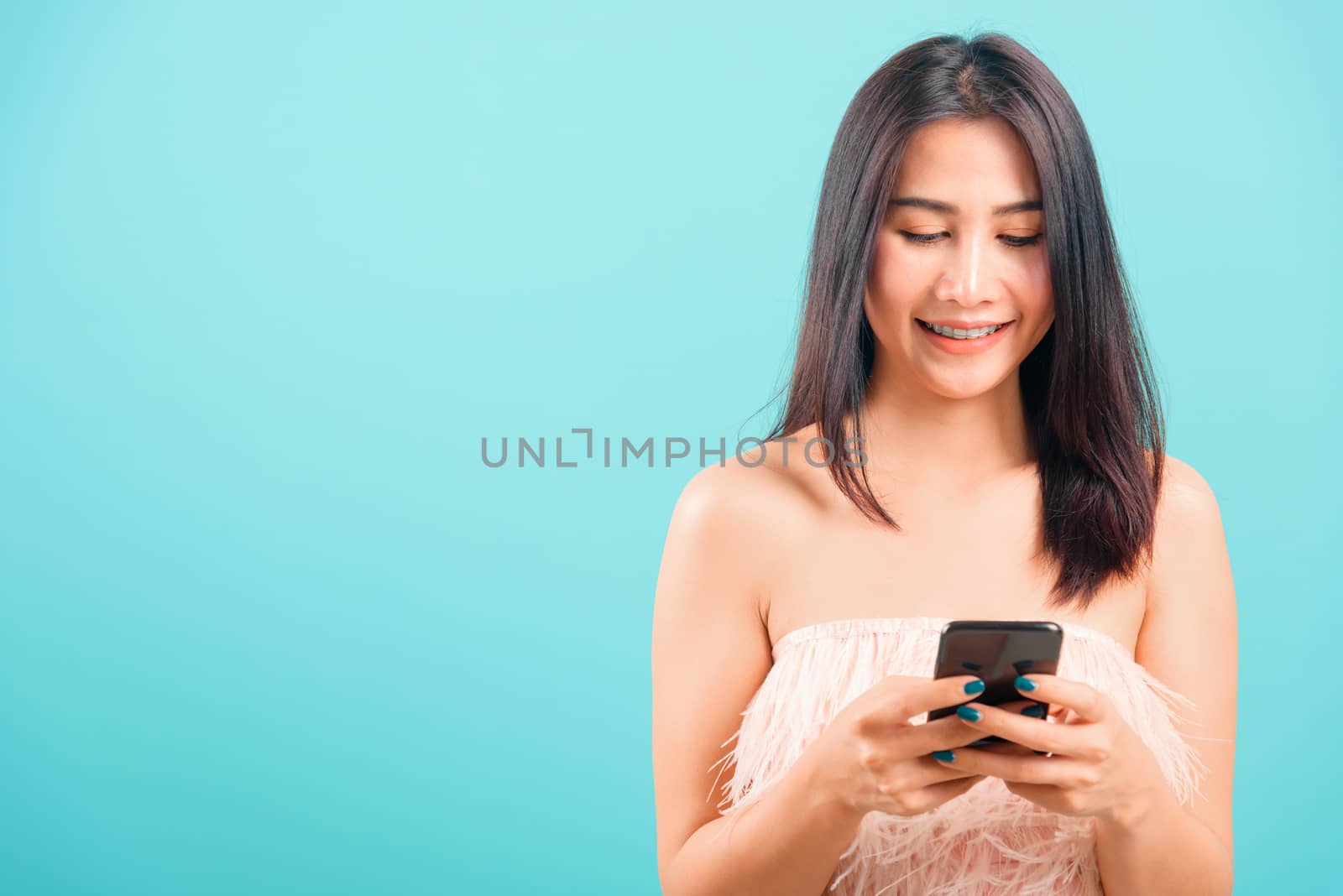 Portrait asian beautiful woman her typing message and smiling on blue background, with copy space for text