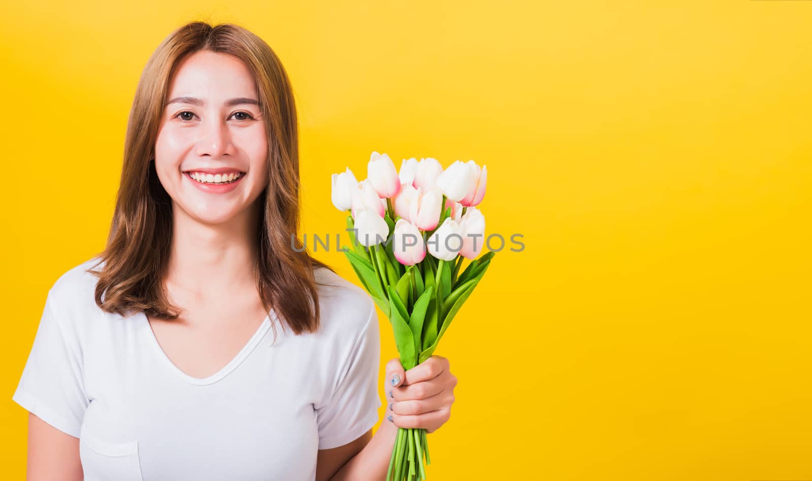 Portrait Asian Thai beautiful happy young woman smiling, screaming excited hold flowers tulips bouquet in hands and looking to camera, studio shot isolated on yellow background, with copy space