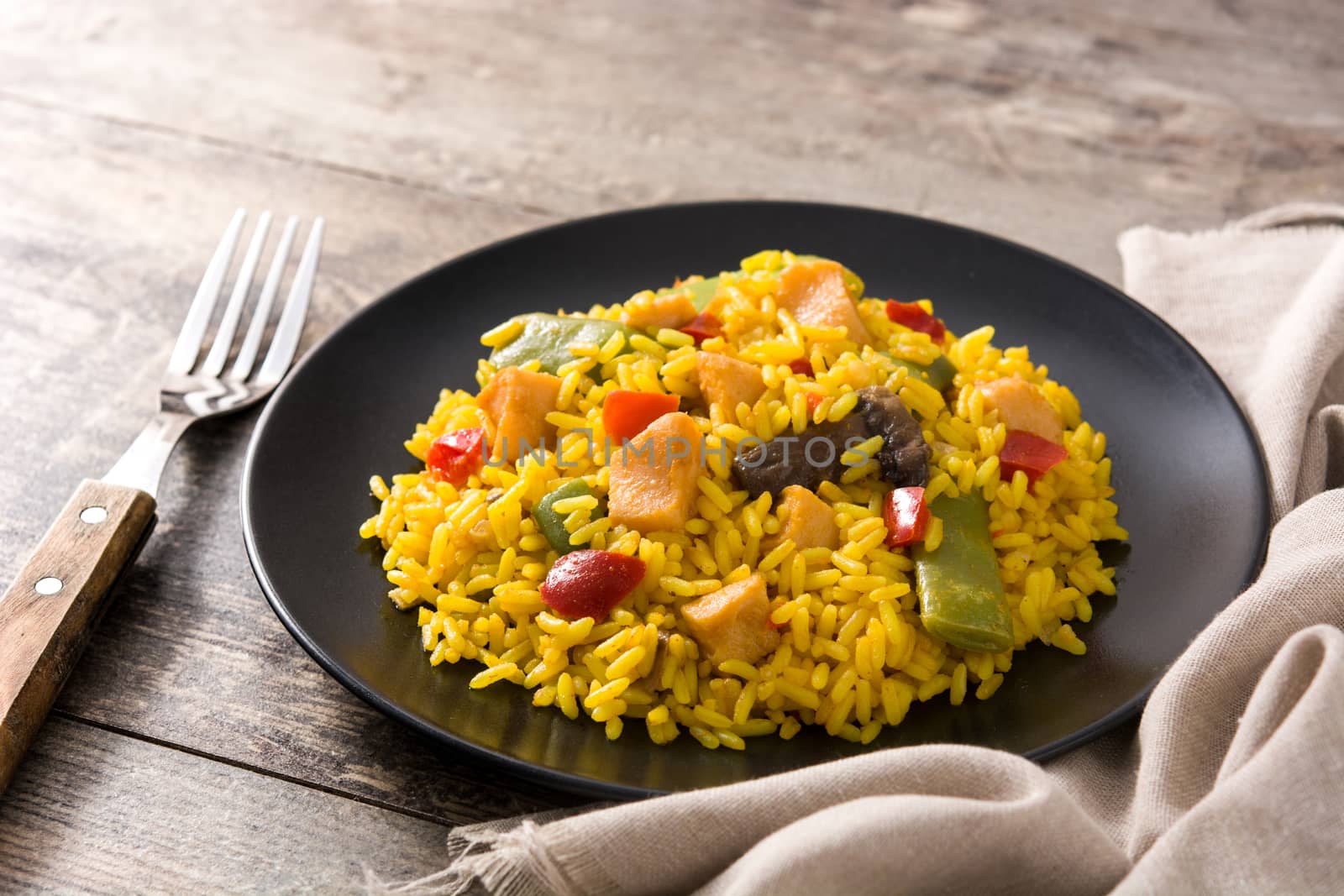 Fried rice with chicken and vegetables on black plate on wooden background