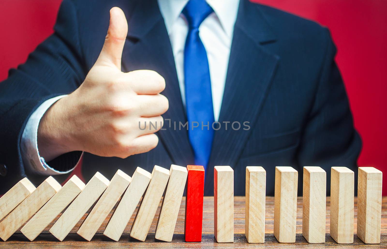 A businessman shows a thumbs up approval over a stopped process falling domino. Find a way stop the problem and prevent its spread. Achieving success and completing a task. Solution. Cyber protection by iLixe48