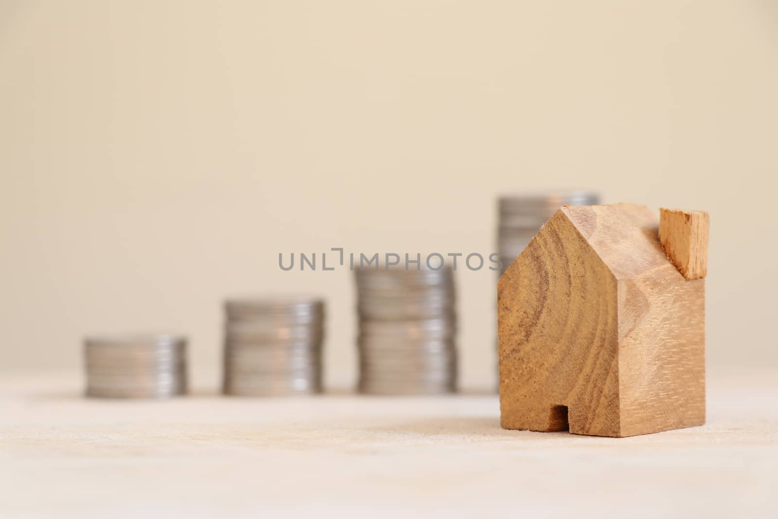 Wooden home model with blurred coins bar graph background.