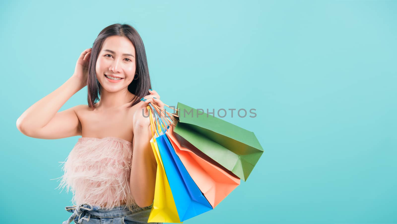 Asian happy portrait beautiful young woman standing smile in summer shopping her holding multicolor shopping bags on hand and looking to camera on blue background with copy space for text