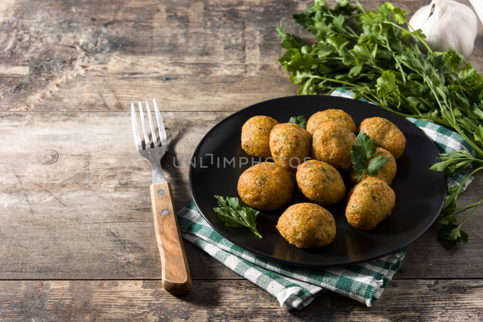 Traditional cod fritters decorated with garlic and parsley on wooden table