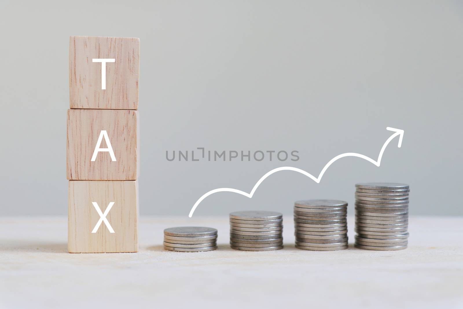 The letter "TAX" on a wooden cube and coins are arranged in a bar graph with growing arrow symbol.