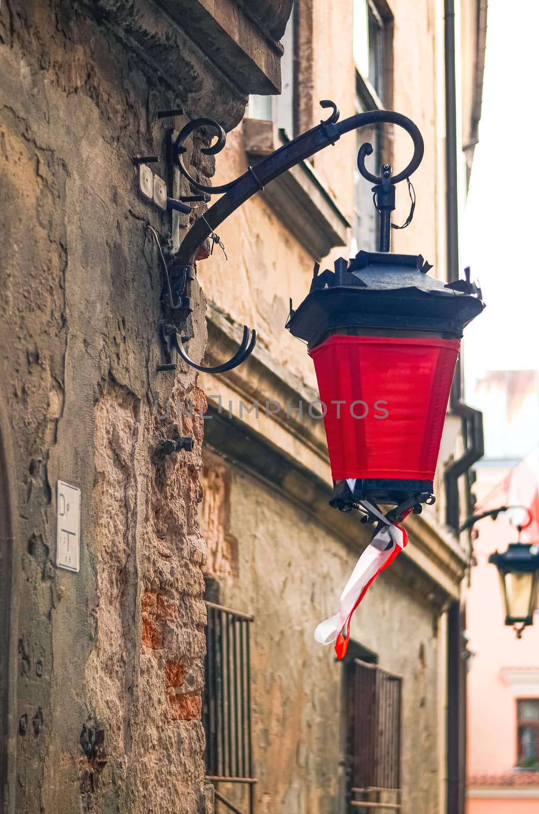 Fragment of an ancient wall with an old street lamp with red cloth and ribbons with national Polish colors in Lublin, Poland