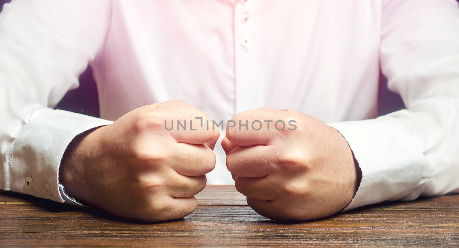 A man holds his closed fists on the table. An attack of anger, stress. A decisive, emotional gesture. Impulsive men. To suffer defeat, failure and loss. End of patience. It is impossible to bear it. by iLixe48