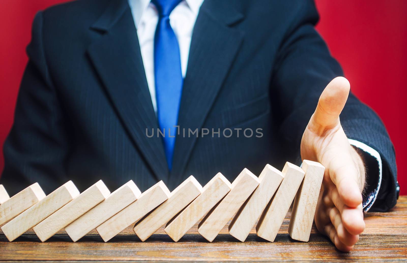 Businessman stops domino falling with his palm. Risk management concept. Successful strong business and problem solving. Stop the destructive processes. Strategy development. Debt restructuring
