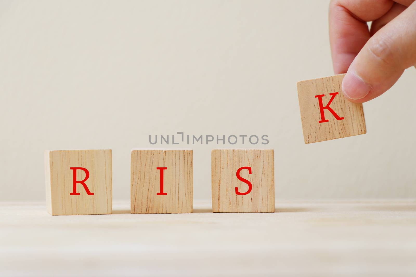 The word "risk" on the wooden cube with hand holding the letter K.