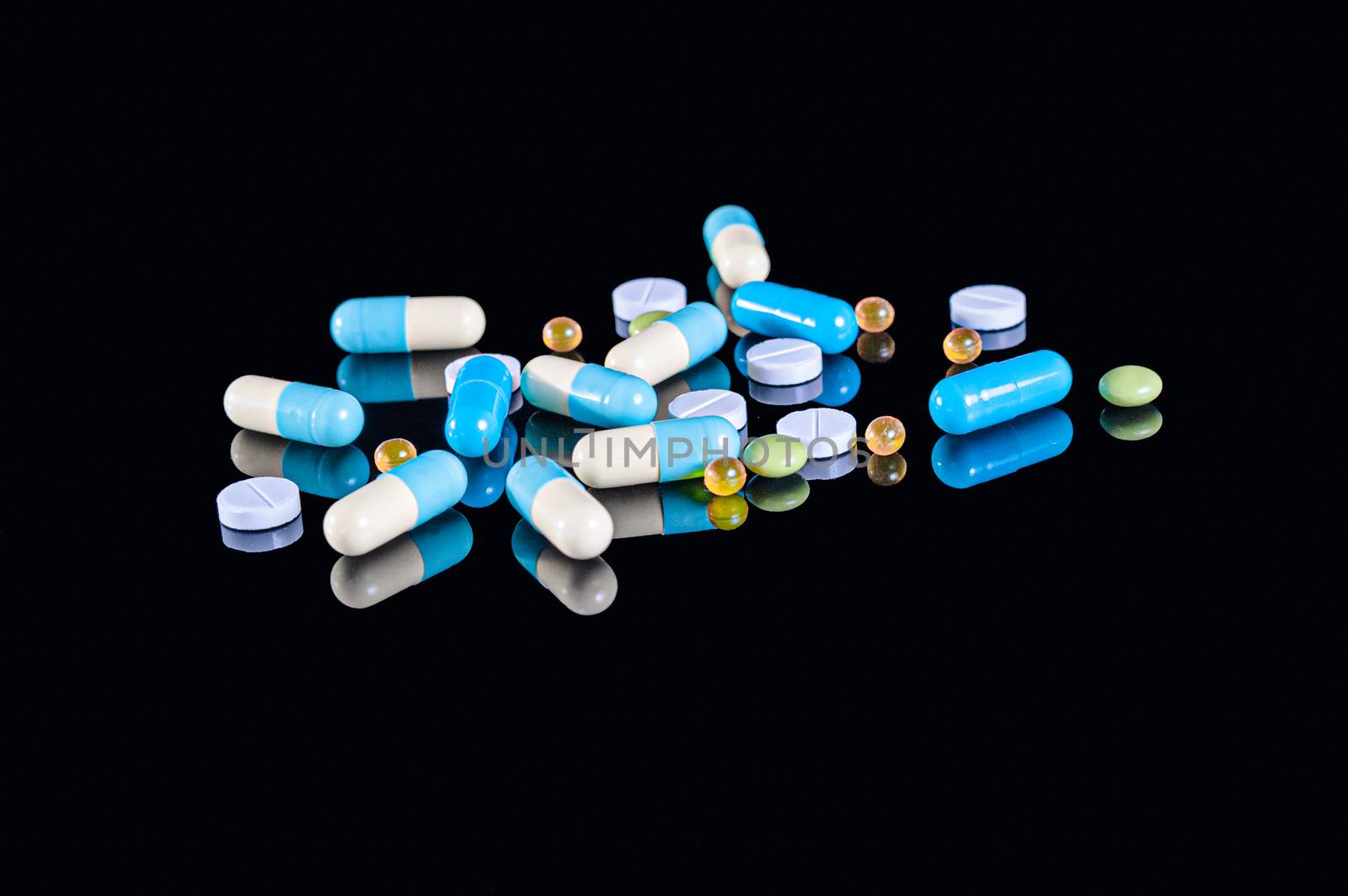 Different tablets, pills and capsules of different colors on an isolated black background with reflection