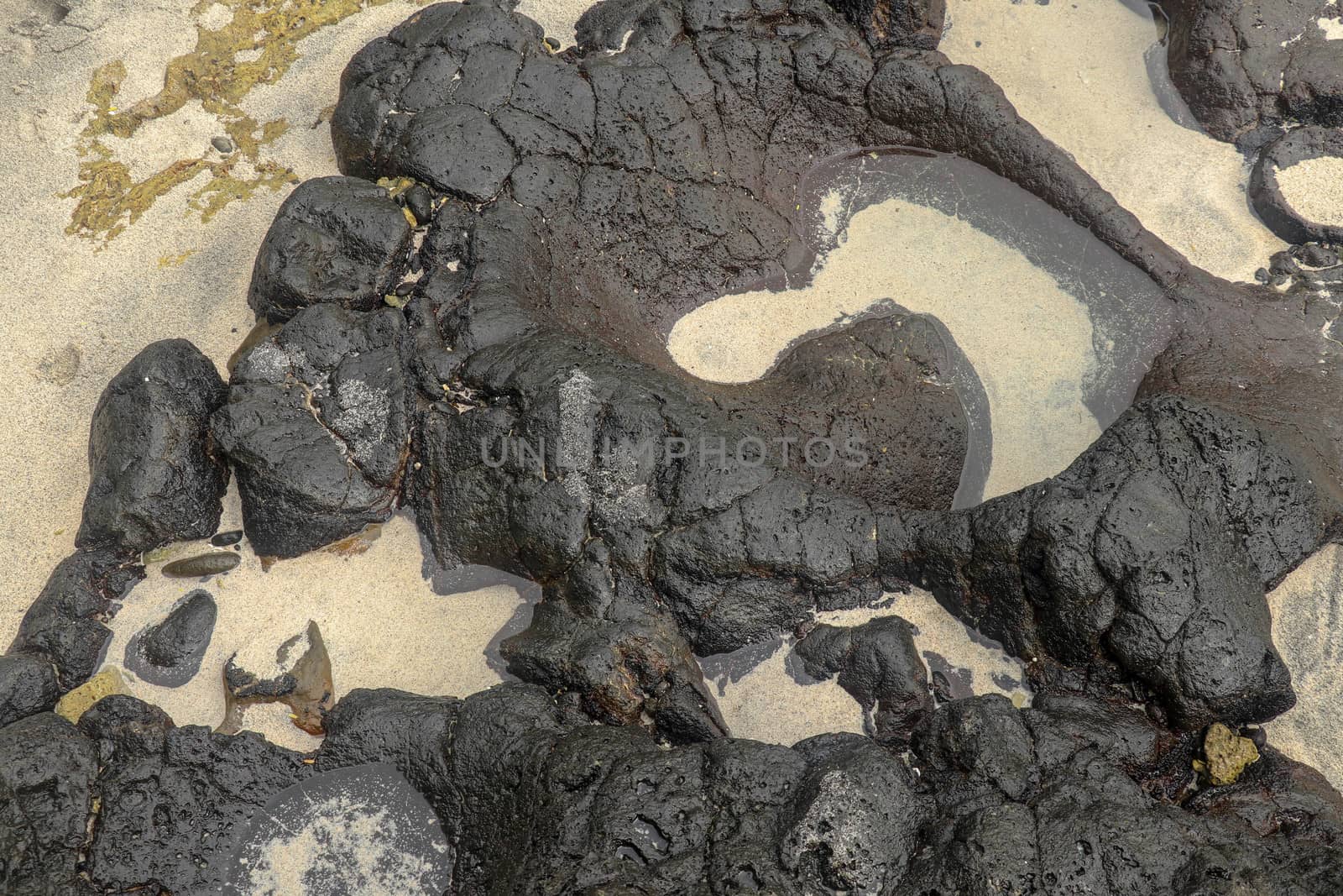 Depressions in a rock with white sand at the bottom, flooded with sea water. Small ponds excavated in lava bed on Indian Ocean coast, Bali, Indonesia. The tide dug out small lakes in the black rock.