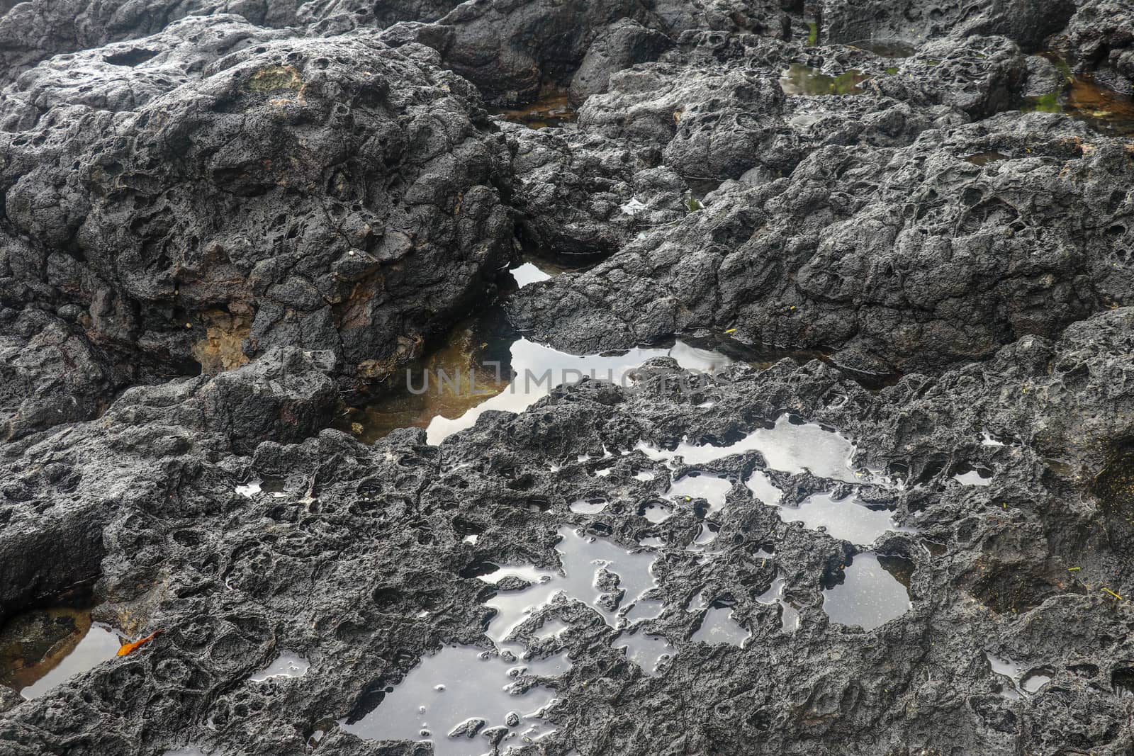 Depressions in a rock with white sand at the bottom, flooded with sea water. Small ponds excavated in lava bed on Indian Ocean coast, Bali, Indonesia. The tide dug out small lakes in the black rock.