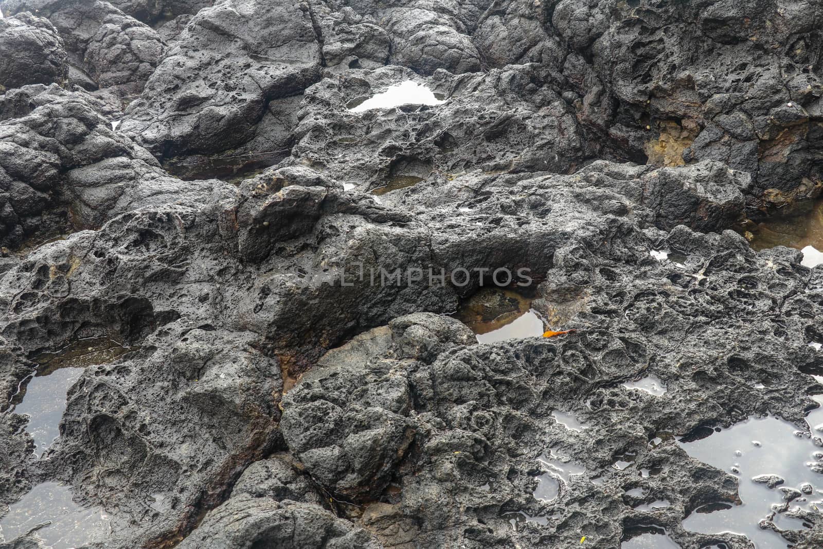 Depressions in a rock with white sand at the bottom, flooded with sea water. Small ponds excavated in lava bed on Indian Ocean coast, Bali, Indonesia. The tide dug out small lakes in the black rock.