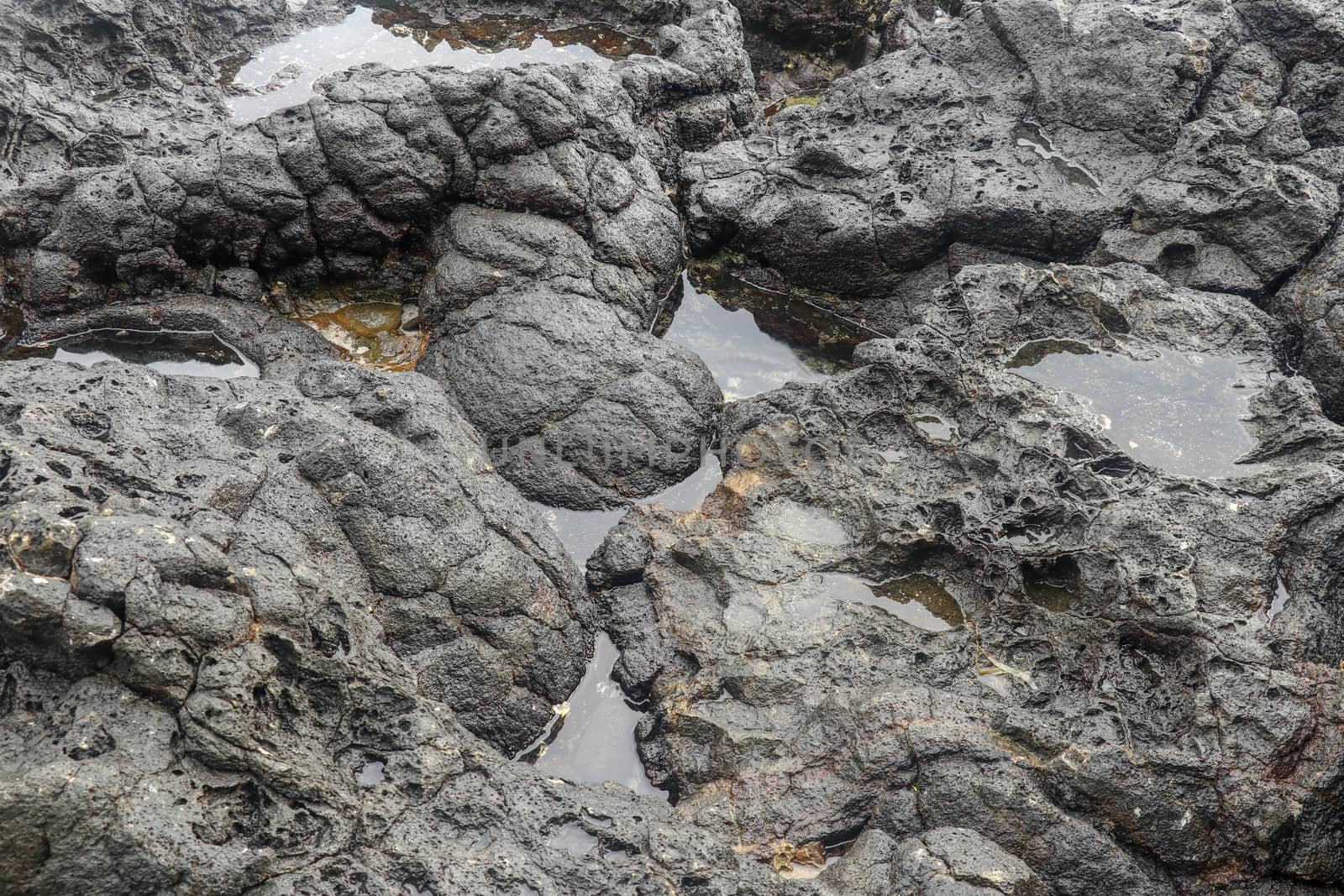 Depressions in a rock with white sand at the bottom, flooded with sea water. Small ponds excavated in lava bed on Indian Ocean coast, Bali, Indonesia. The tide dug out small lakes in the black rock.