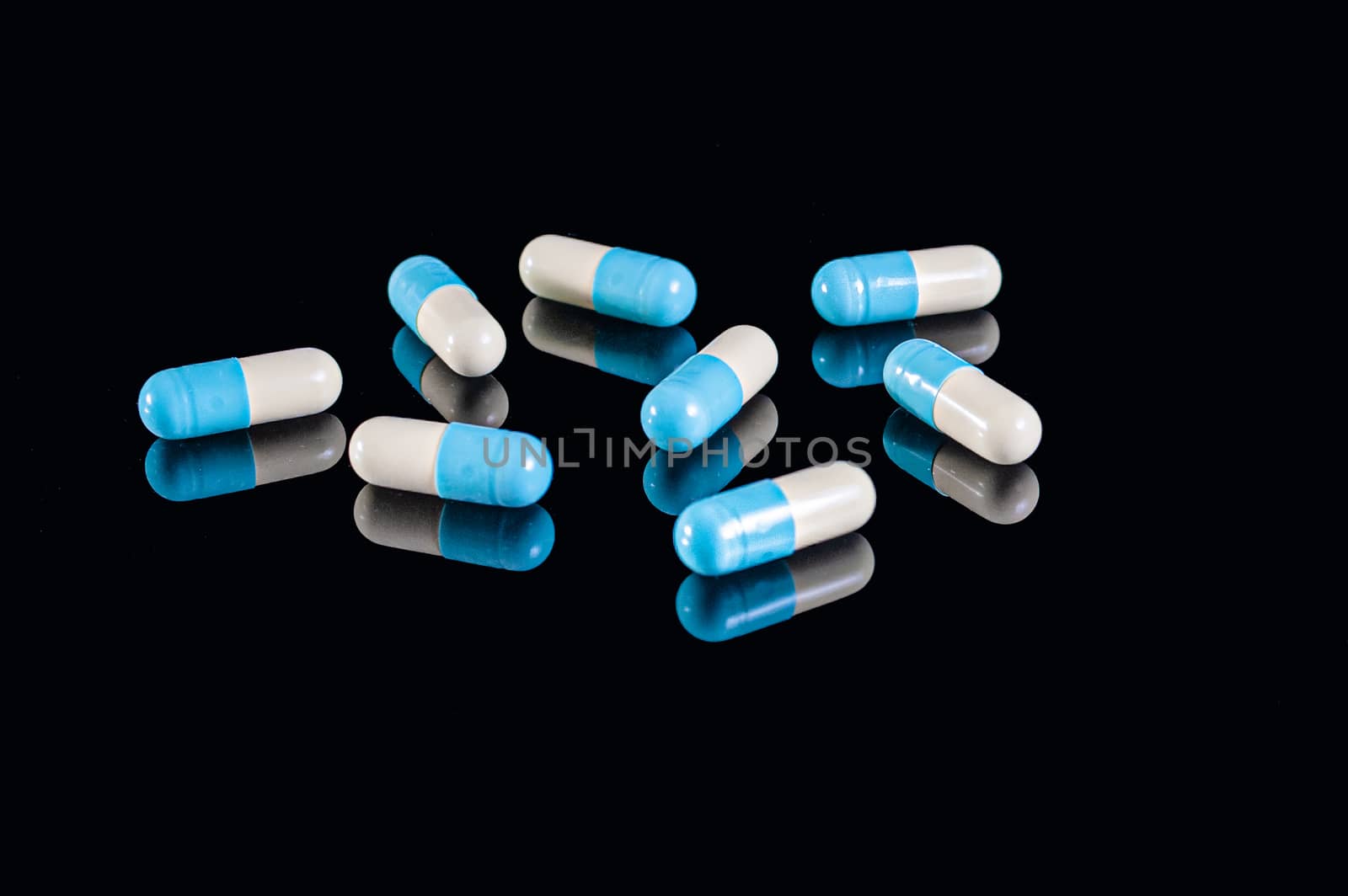 White and blue two halves capsules on an isolated black background with reflection
