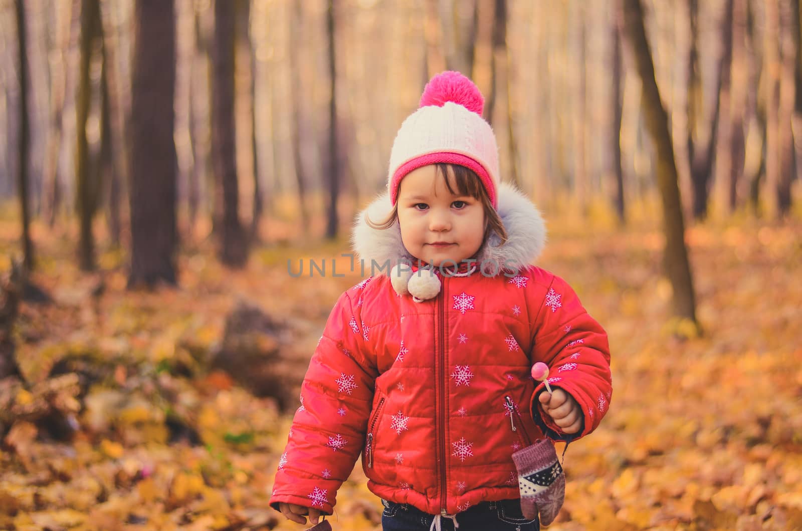 beautiful girl in winter clothes with lollipop in the autumn park by chernobrovin