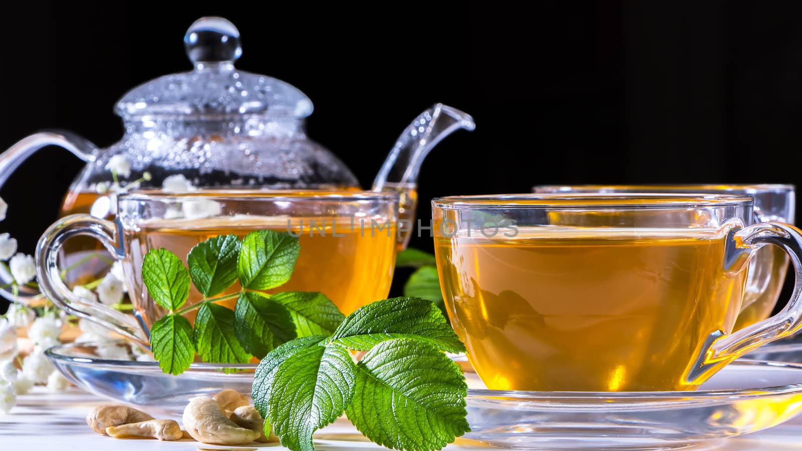 Teapot and mugs with green tea, cashew nuts, green leaves and wh by YevgeniySam