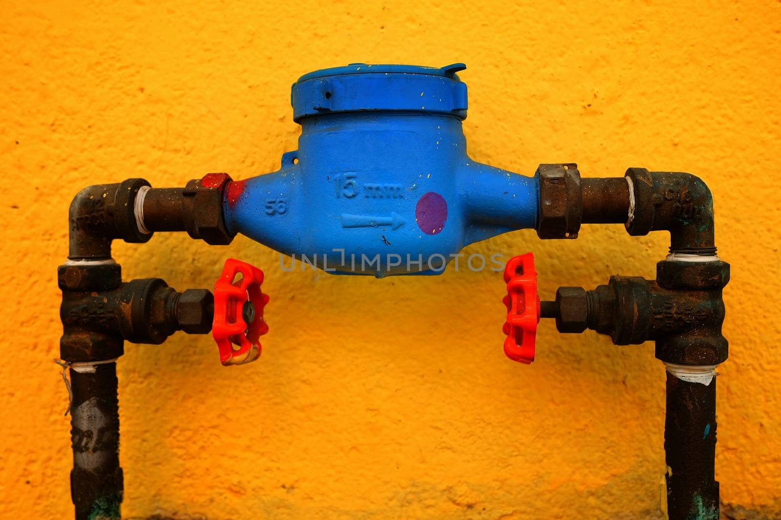 Old Blue Water Meter With Yellow Painted Concrete Wall Background. by mesamong