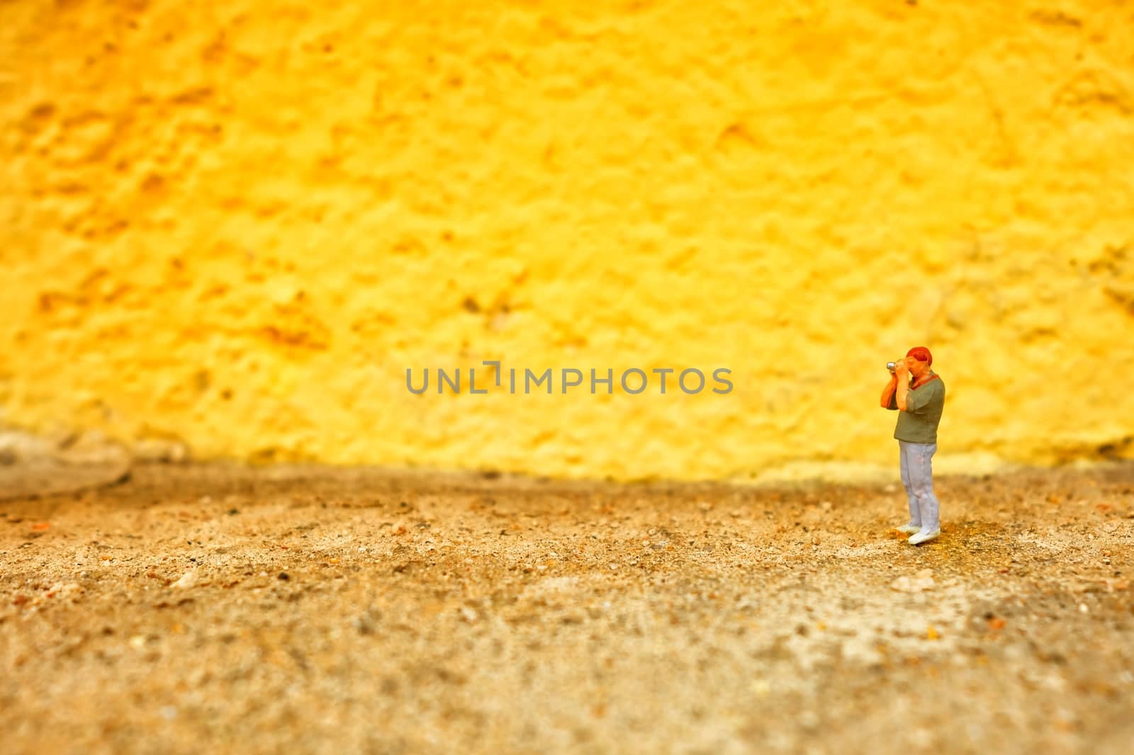 Miniature Figure Photographer with Yellow Painted Concrete Wall Background.