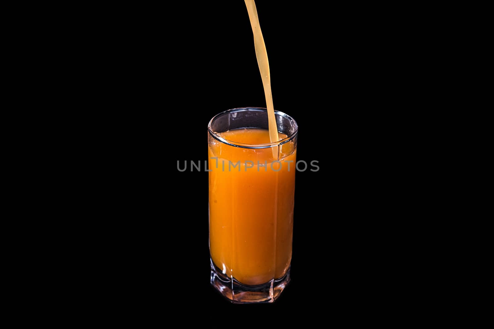 Freshly squeezed fruit juice is poured into a glass. Peach, orange or carrot on an isolated black background. by chernobrovin