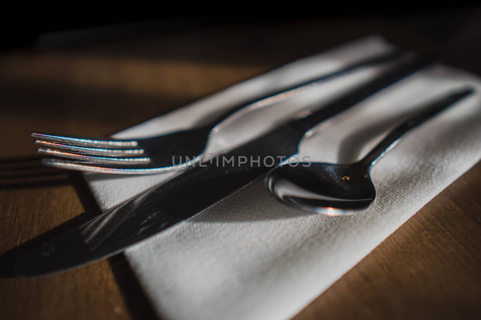 Some silverware, cutlery sat on a white napkin on a wooden table in a cafe setting