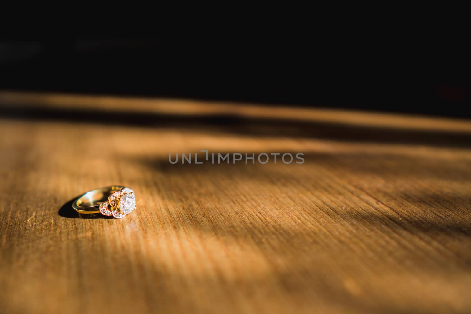 A gold diamond engagement ring sat on a wooden table in natural daylight