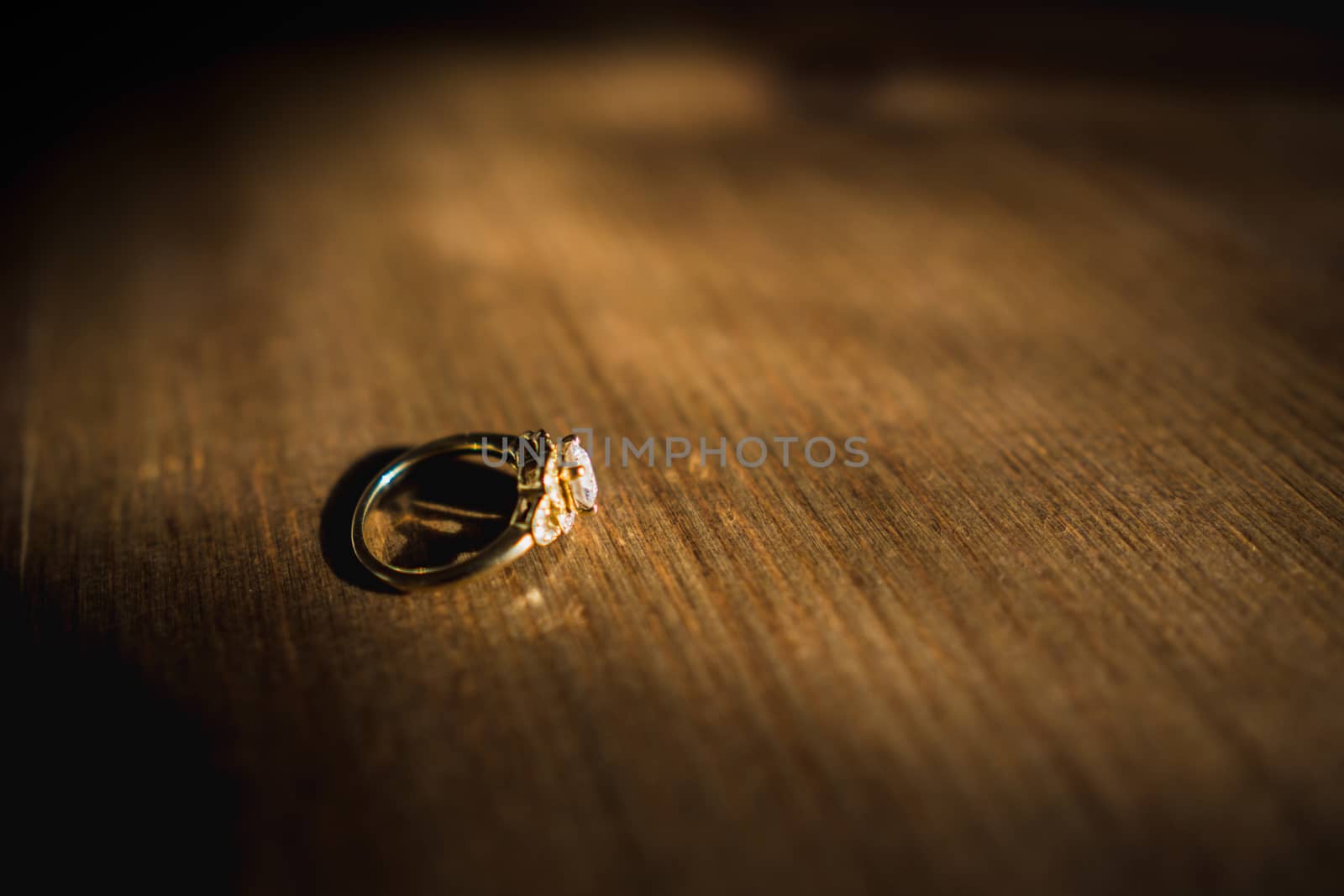 A gold diamond engagement ring sat on a wooden table in natural daylight