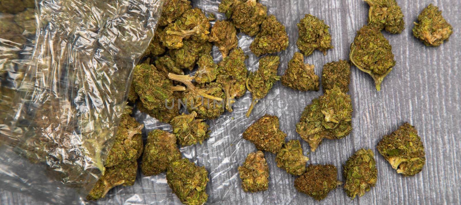 Large buds of medicinal marijuana pour out of a clear plastic bag. Sitting on wooden surface.