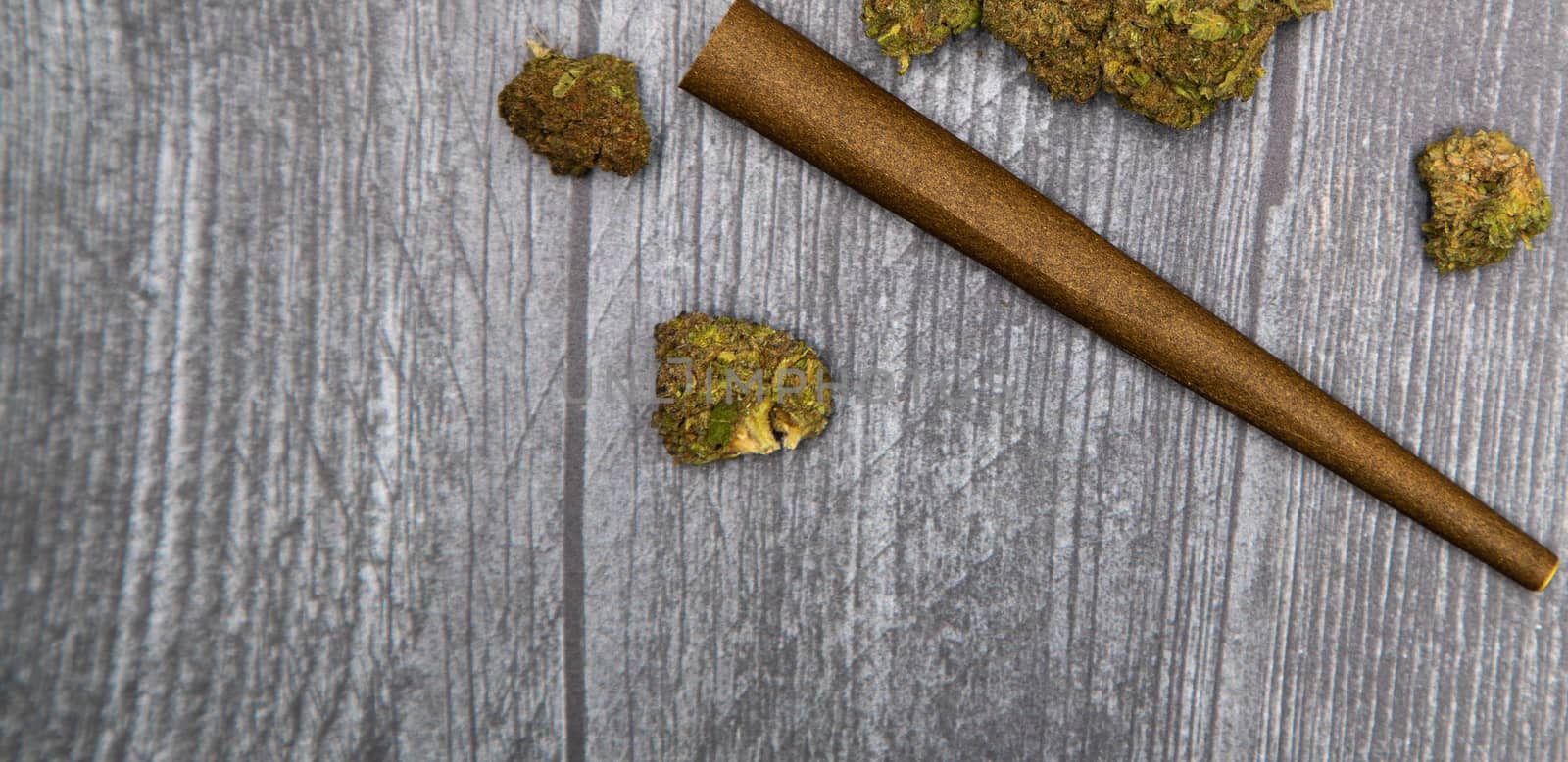 Several buds of medicinal marijuana sit on a wooden surface next to a CBD infused hemp wrap.