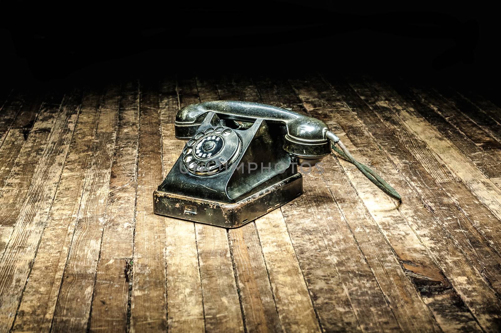 black retro telephone with a rotary dial stands on a wooden floor in the dark