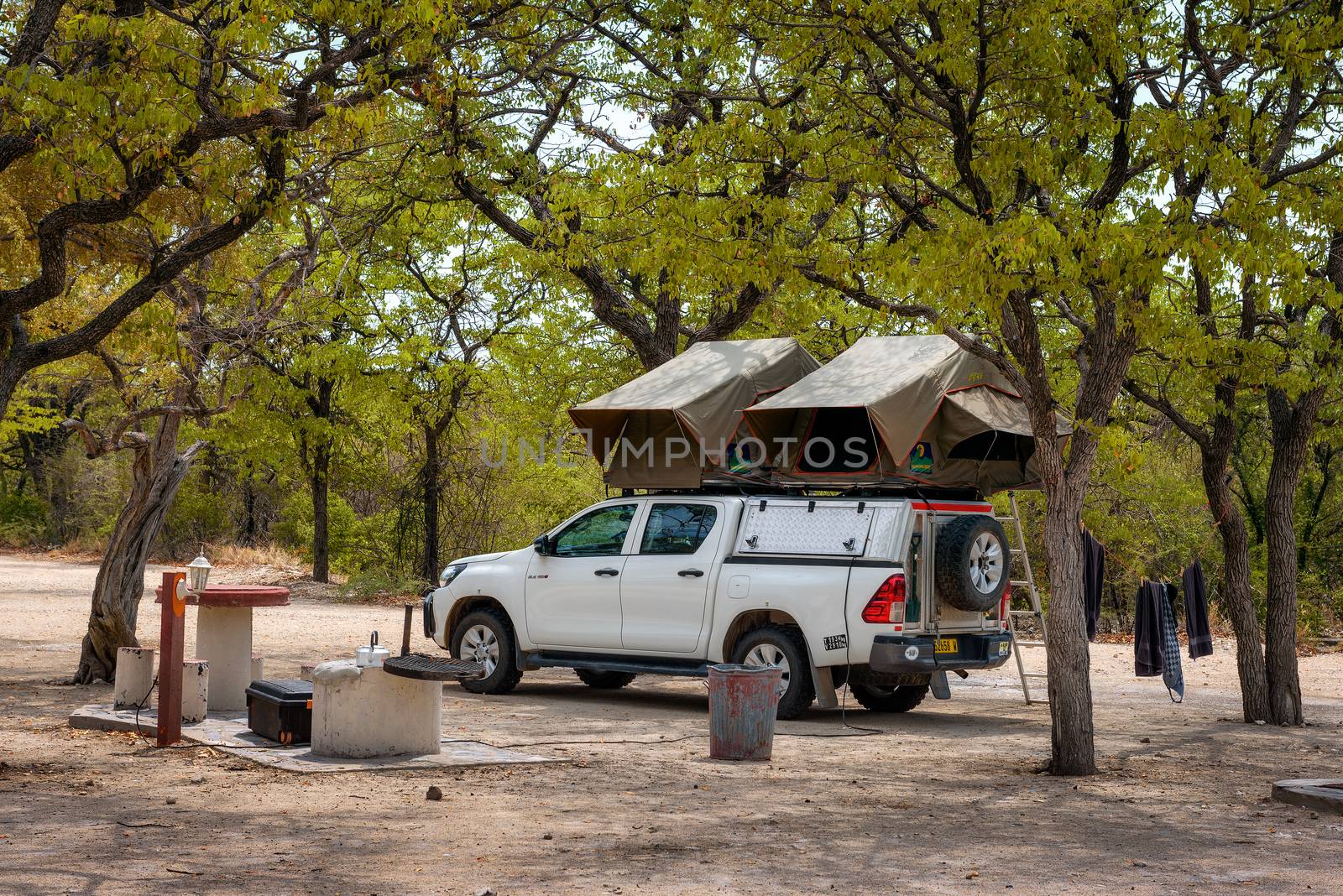Halali, Namibia - March 27, 2019 : Tent located on the roof of a pickup 4x4 car parked under trees of Halali camp in Etosha National Park.