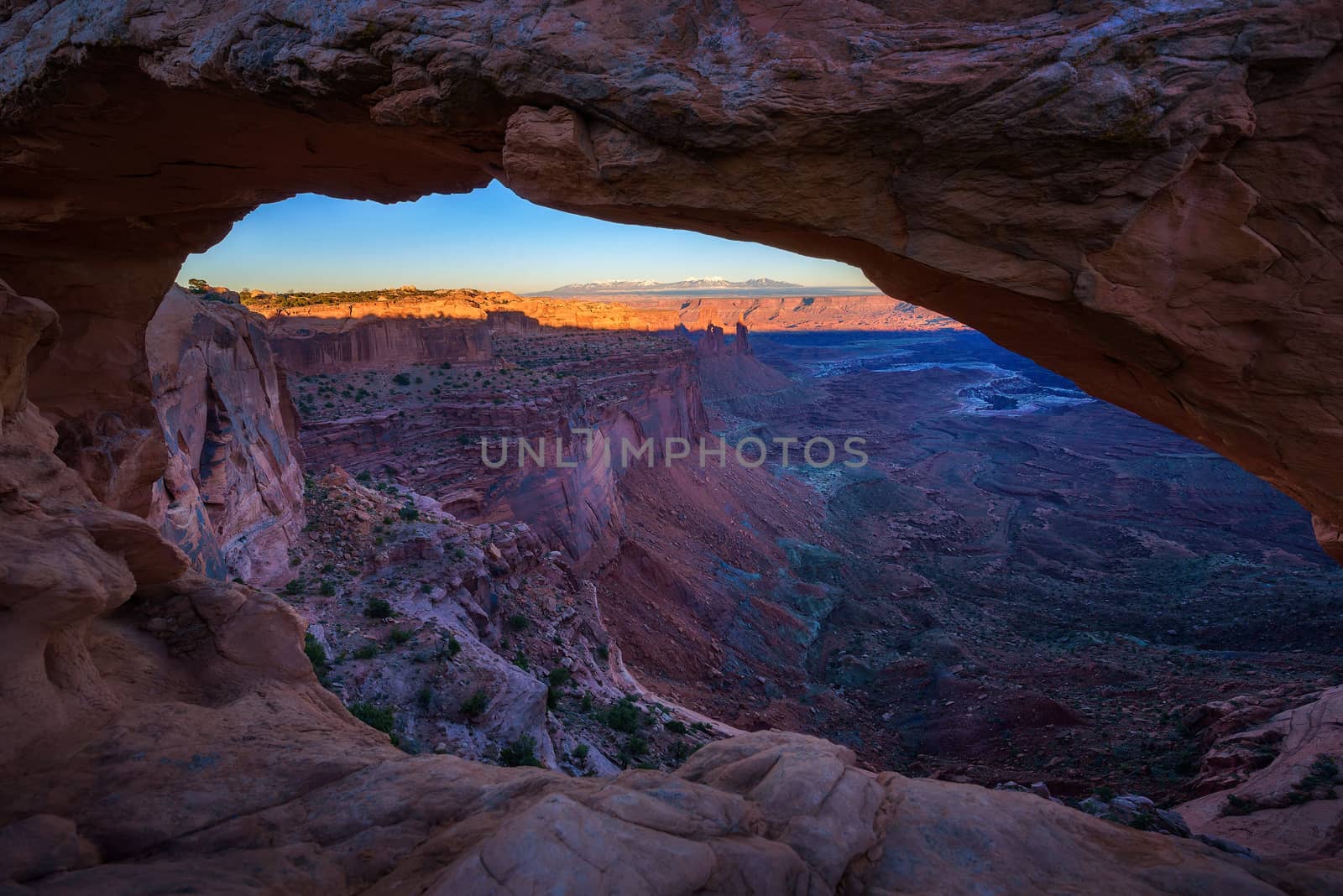 Sunset viewed through the Mesa Arch in Canyonlands National Park near Moab, Utah with snow covered Rocky Mountains in the background. Mesa Arch became a symbol of the American Southwest.