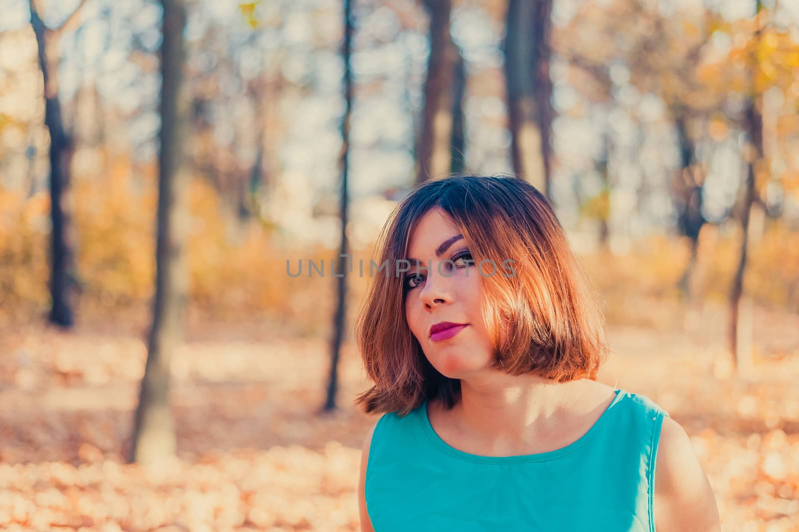 cute young red-haired girl with beautiful eyes in a blue dress looks at the camera in the autumn yellow forest by chernobrovin