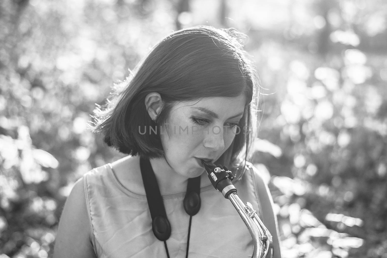 bw portrait of a young brunette girl playing the saxophone outside by chernobrovin