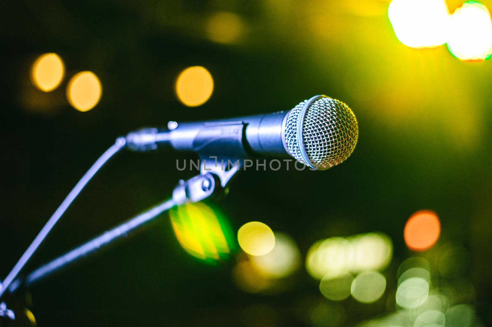 singer's vocal microphone stands on stage during a concert with multi-colored lights on the background