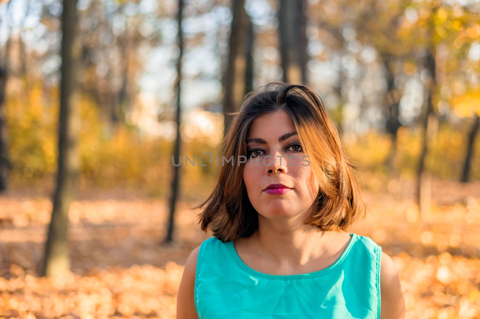 pretty dark-haired girl with makeup and red lips in blue clothes in the autumn yellow forest