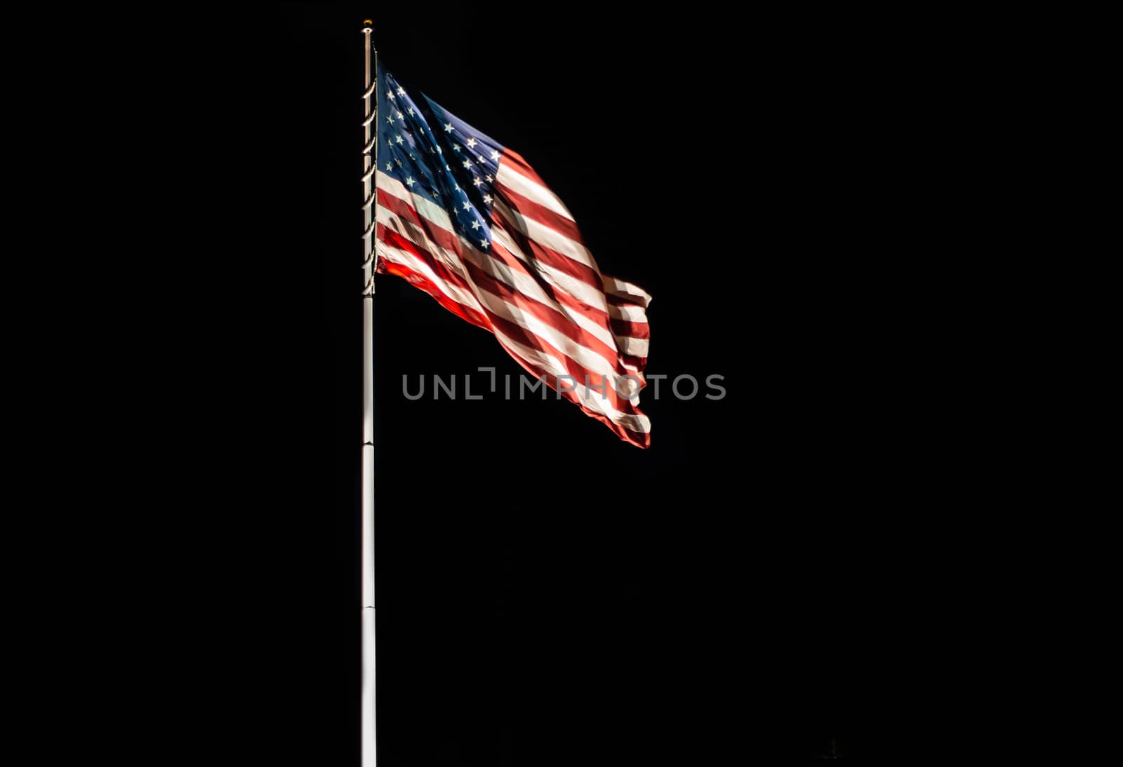 Pole with waving Old Glory American flag isolated on a pure black expandable background with copy space