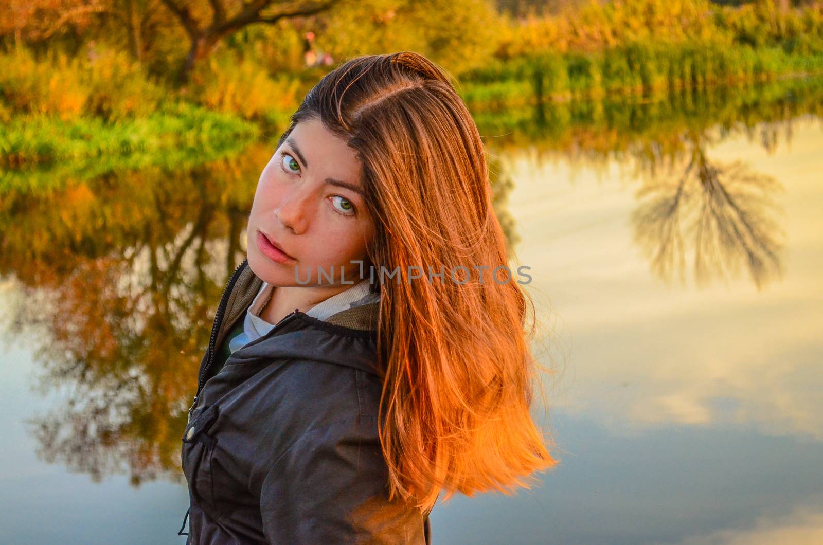 Beautiful young girl standing near lake in autumn