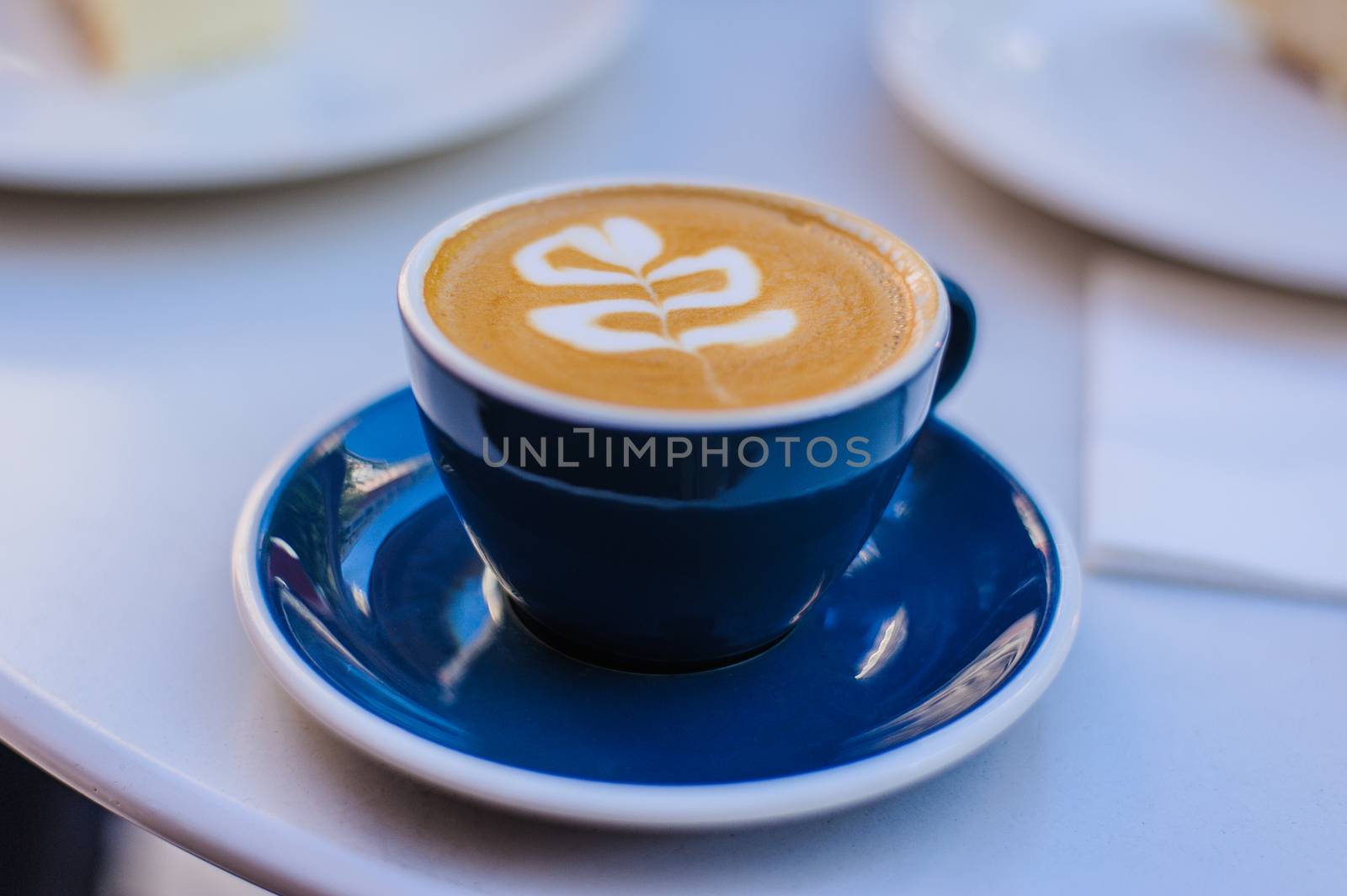 aromatic coffee cappuccino in a blue cup on a saucer stands on a white table