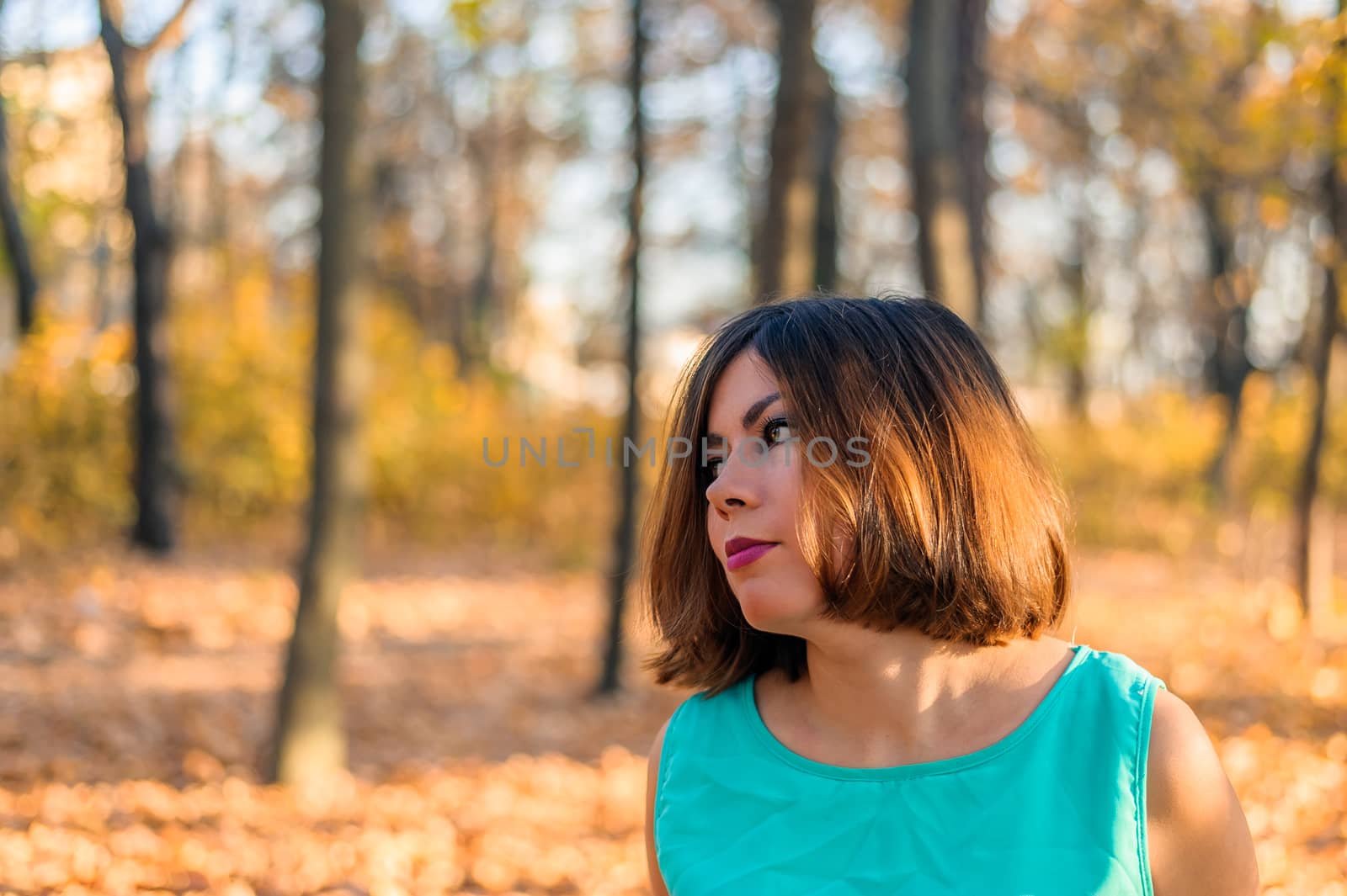 close portrait of a young woman with dark hair who looks away while standing in an autumn park