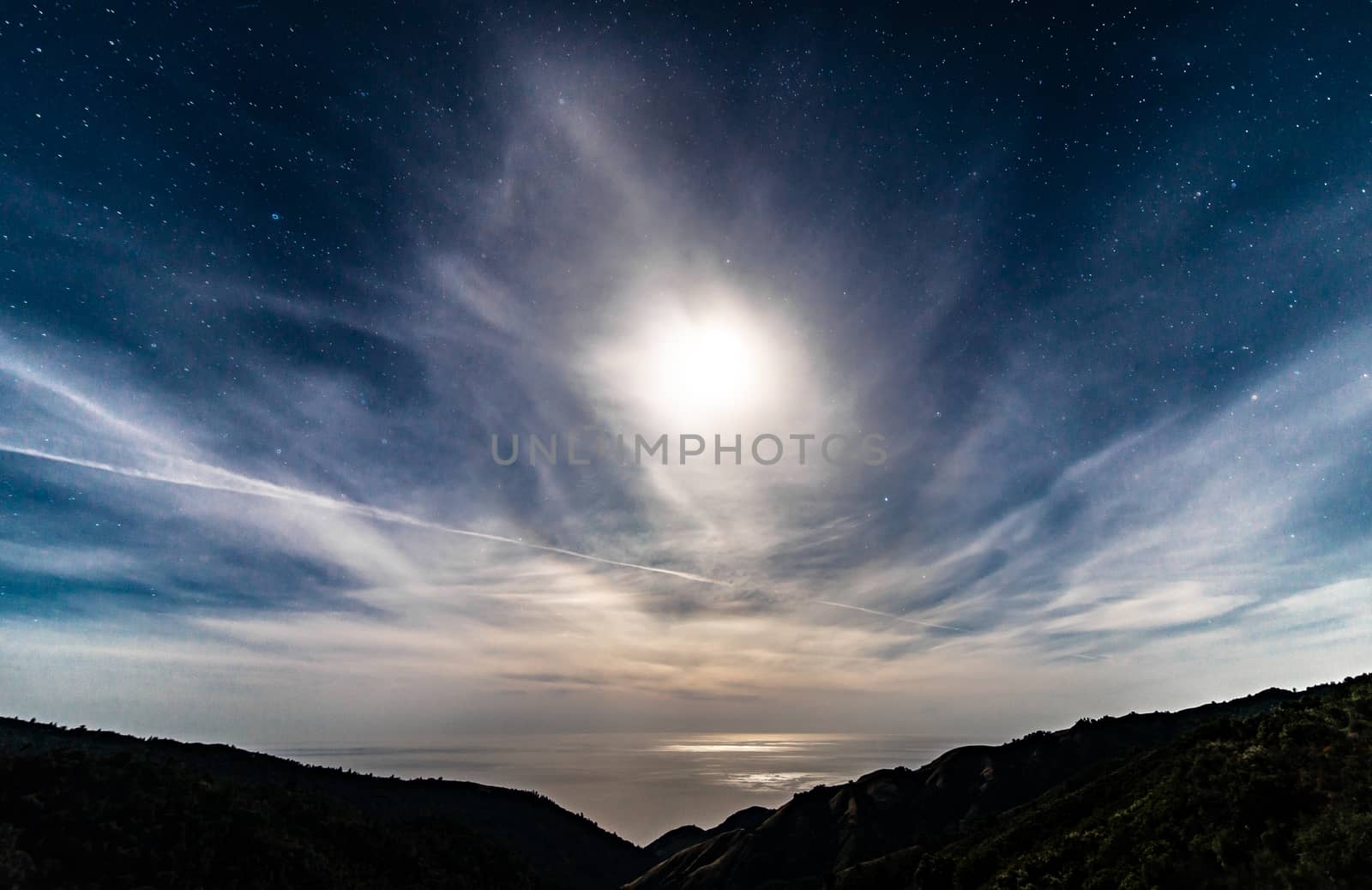 Moonlit California starry night sky over the ocean with full moon behind clouds by Pendleton